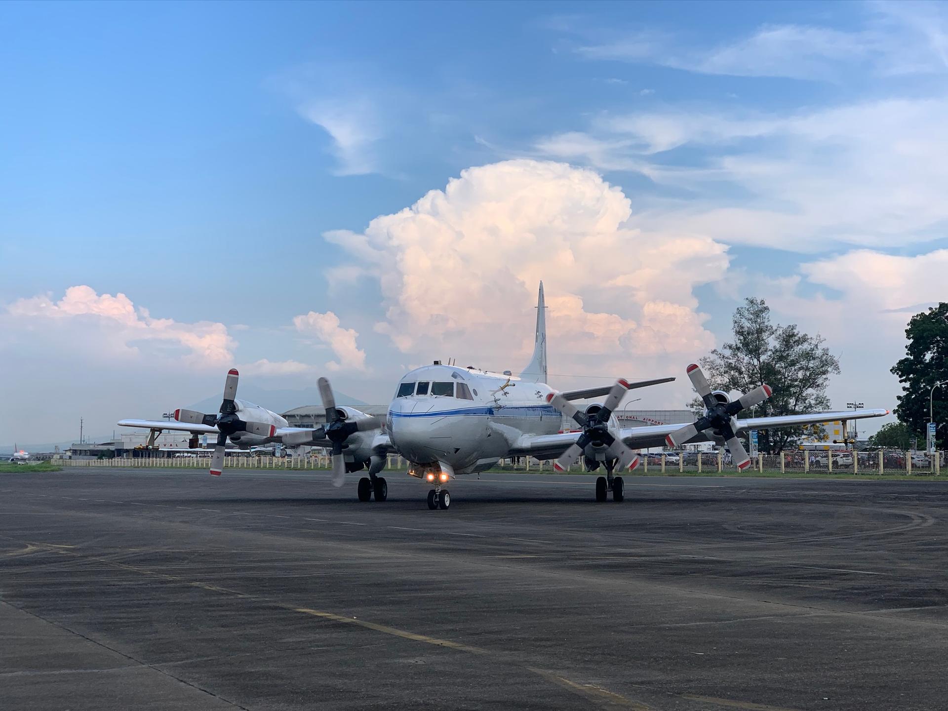Image of a NASA P-3 Orion aircraft on the tarmac with a large storm in the background.